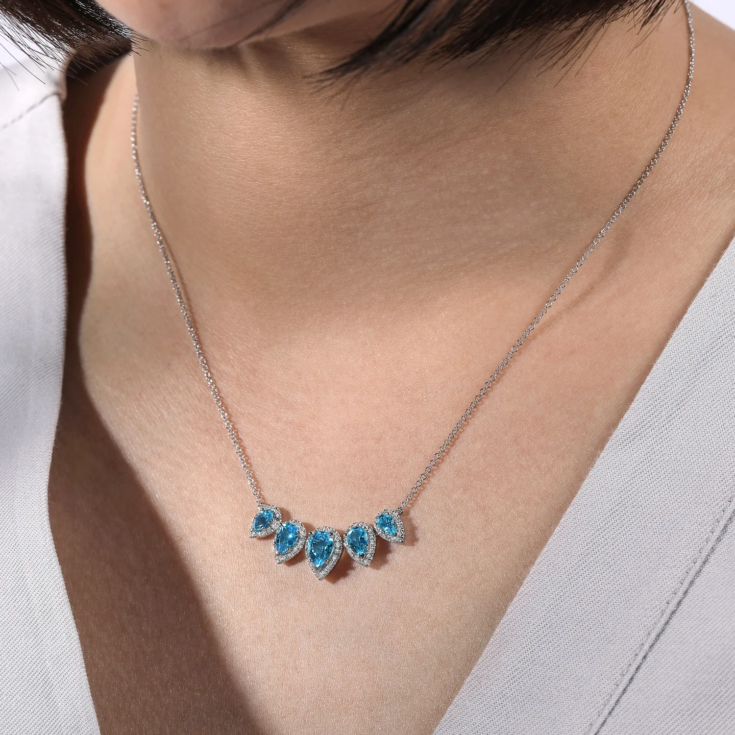 Graduating Pear Shaped Blue Topaz and Diamond Halo Necklace in 14K White Gold, photograph 3